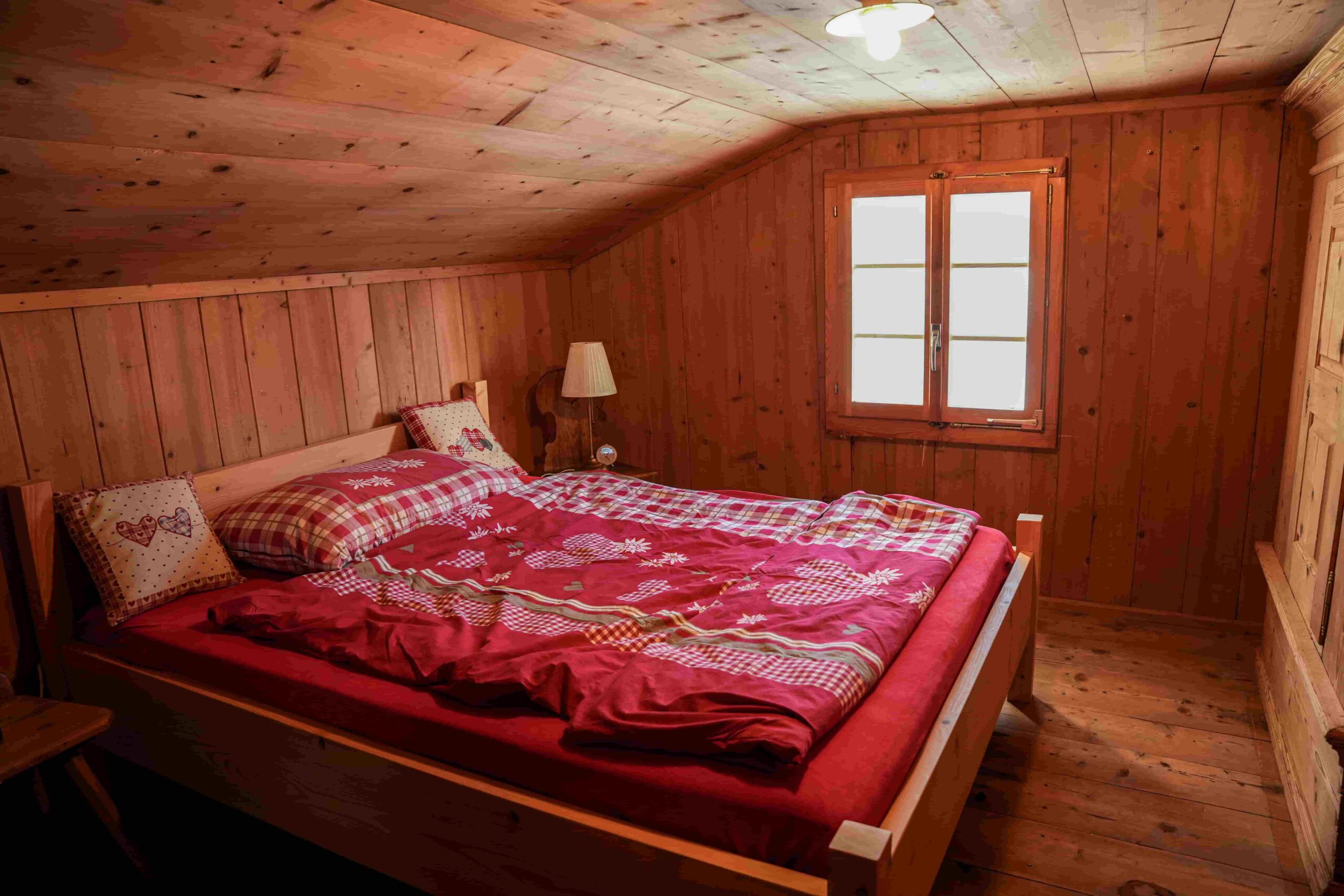 Un lit dans un chalet d'alpage avec une housse de lit rouge.