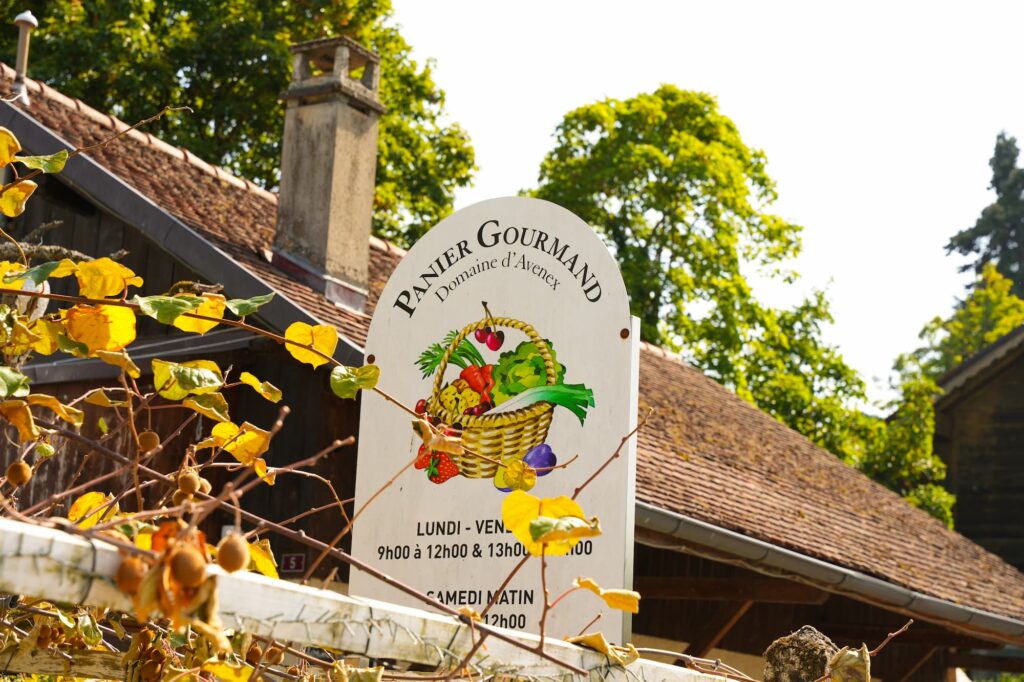 Un panneau blanc avec le logo de la ferme, derrière lequel on aperçoit un toit.